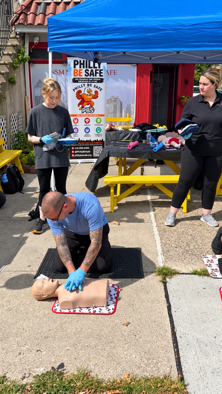 Outdoor Philly Be Safe CPR demonstration with an adult practicing chest compressions on a training manikin